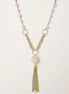 Layered gold-plated necklace with freshwater pearls, central pearl cluster, and chain tassel on cream background.
