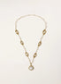 Long gold-plated necklace with eye-shaped elements, freshwater pearls, and baroque pearl pendant on neutral background.