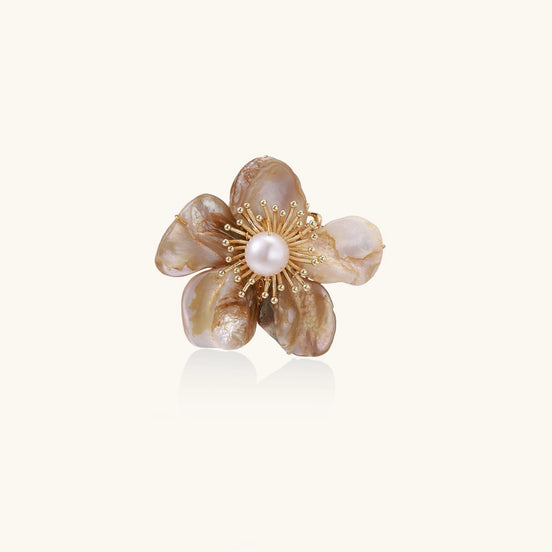 Elegant floral pin with peachy shell petals, gold radiating spokes, and white freshwater pearl center on cream background.