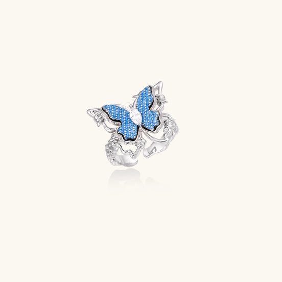 Gold-plated brass ring featuring blue butterfly design with central zirconia stone on neutral background.