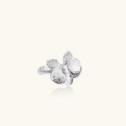 Gold-plated brass ring with textured orchid petals, zirconia stones, and center pearls on white background.