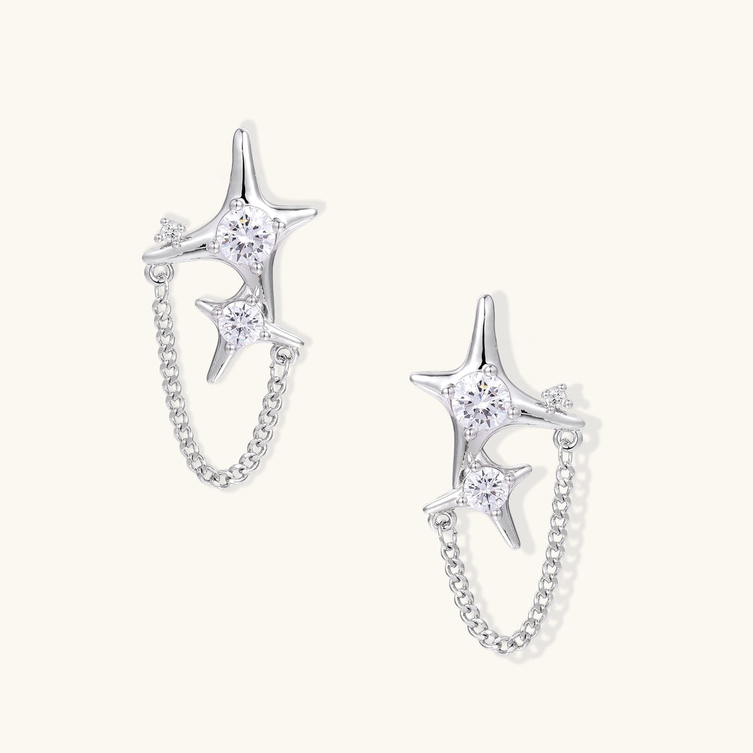 Delicate gold-plated star earrings with sparkling zirconia crystals connected by fine chains on cream background.