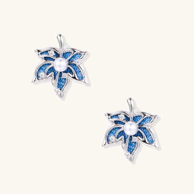 Silver-toned floral earrings with blue denim fabric petals, white pearls, and crystal accents on cream background.