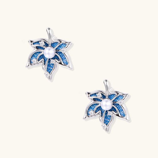 Silver-toned floral earrings with blue denim fabric petals, white pearls, and crystal accents on cream background.