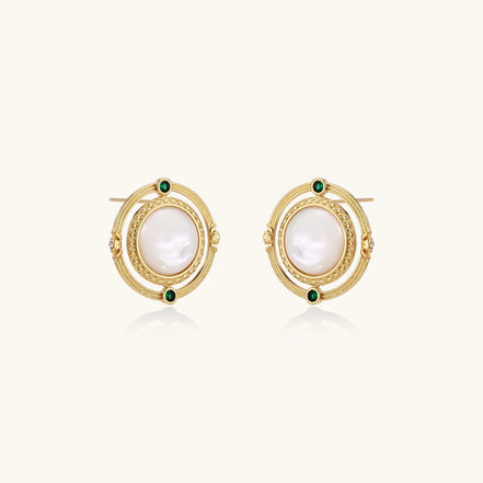Close-up of gold-plated circular earrings with white mother-of-pearl centers and green zirconia accents on cream background.