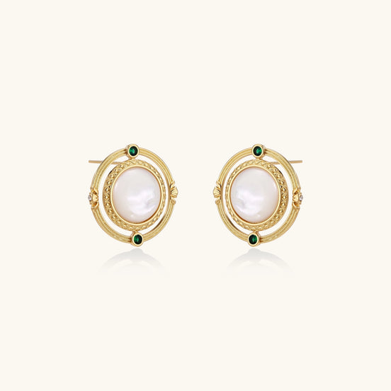 Close-up of gold-plated circular earrings with white mother-of-pearl centers and green zirconia accents on cream background.