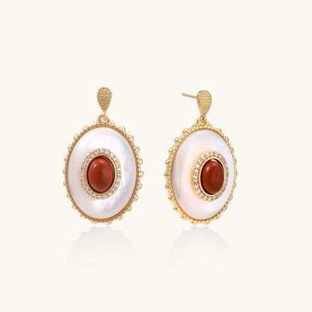 Gold-plated drop earrings with oval mother-of-pearl stones, central red gemstones, and crystal accents on white background.