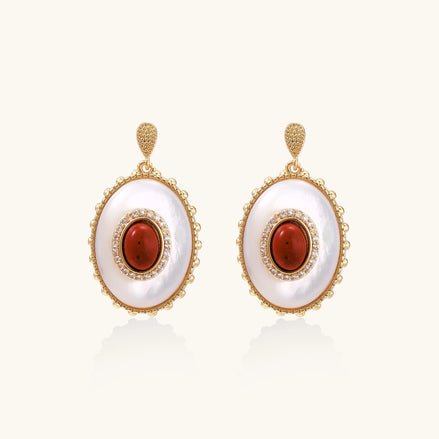Gold-plated drop earrings with oval mother-of-pearl stones, central red gemstones, and crystal accents on white background.
