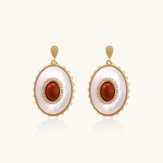 Gold-plated drop earrings with oval mother-of-pearl stones, central red gemstones, and crystal accents on white background.