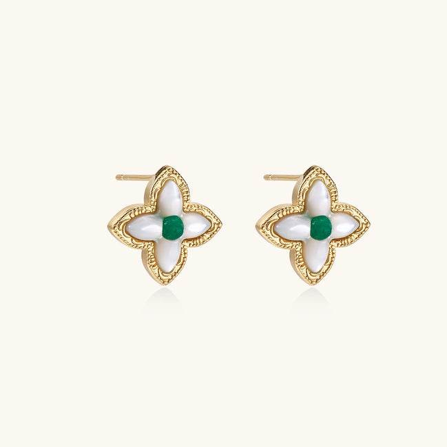 Dainty gold-plated quatrefoil stud earrings with white mother-of-pearl petals and green gemstone centers on beige background.