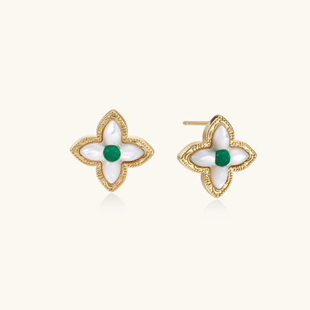 Dainty gold-plated quatrefoil stud earrings with white mother-of-pearl petals and green gemstone centers on beige background.