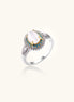 Gold-plated ring with oval cat's eye stone center, blue accent stones, and crystal halo on white background.