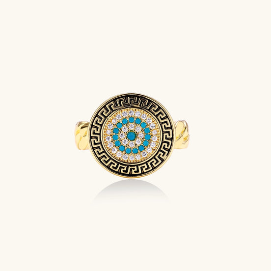 Gold-plated brass ring with Greek key border, evil eye center, and turquoise cubic zirconia stones in chunky chain band style.