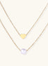 Two delicate gold-plated chains layered together, one with small heart pendant, another with cream pearl bead