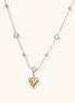 Dainty 14K gold plated necklace with heart pendant and bezel-set crystals on delicate chain against cream background.
