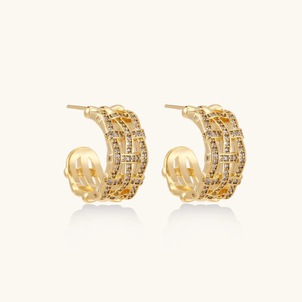 Close-up of geometric gold-plated hoop earrings with crystal pave in intricate lattice pattern on neutral background.