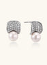 Elegant gold-plated curved earrings with diamond pavé crescents and suspended freshwater pearls on neutral background.