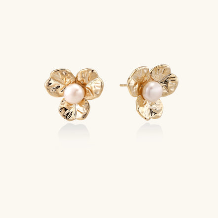 Gold-plated flower stud earrings with freshwater pearl centers on beige background, showing textured petal details.