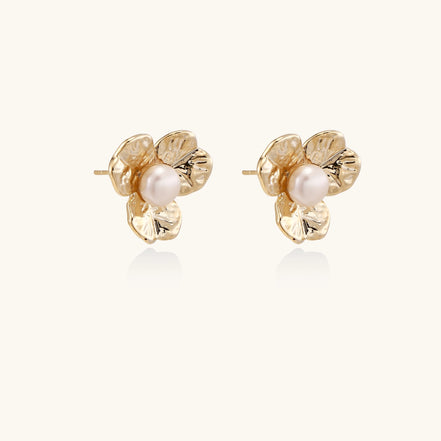 Gold-plated flower stud earrings with freshwater pearl centers on beige background, showing textured petal details.