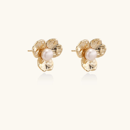 Gold-plated flower stud earrings with freshwater pearl centers on beige background, showing textured petal details.