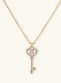 Gold-plated key pendant necklace with heart top and crystal embellishments on adjustable chain against cream background