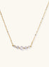 Delicate 14K gold plated necklace with curved arc of sparkling zirconia stones on cream background.