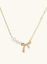 Delicate gold-plated necklace with three white pearls and sparkling bow pendant on cream background.
