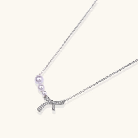 Dainty 14K gold plated necklace with freshwater pearls and sparkling bow charm on white background.