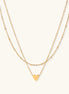 Two-layer gold-plated stainless steel necklace with small heart pendant displayed on beige background