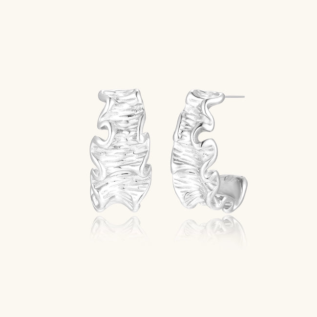 Textured gold-plated hoop earrings with flowing ripple design displayed on clean white background.