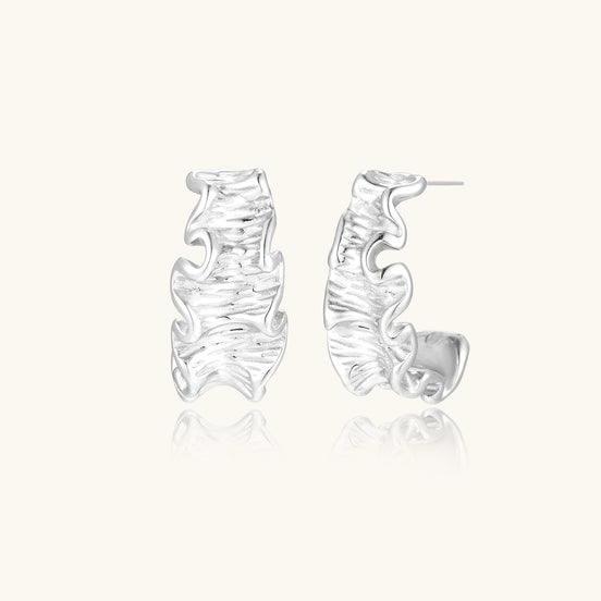 Textured gold-plated hoop earrings with flowing ripple design displayed on clean white background.