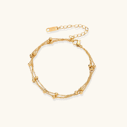 Delicate 18K gold plated bracelet with spherical beads on layered chains and adjustable extender on white background