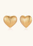 Close-up of ridged heart-shaped gold-plated stud earrings with textured surface pattern on cream background.