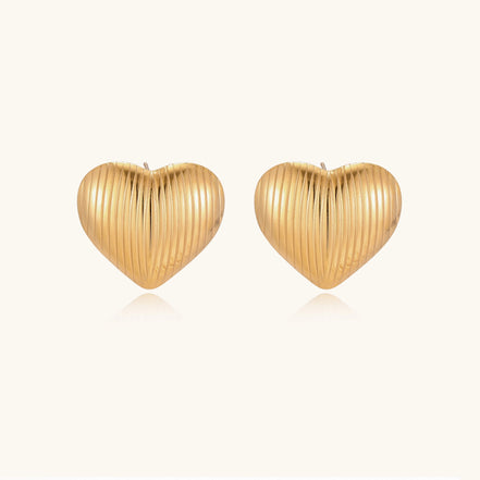 Close-up of ridged heart-shaped gold-plated stud earrings with textured surface pattern on cream background.