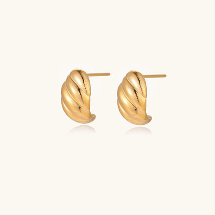 Pair of gold-plated twisted stud earrings with sculptural spiral design displaying elegant curved ridges on cream background.
