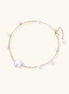 Delicate gold chain bracelet with baroque pearl centerpiece and small freshwater pearls on cream background.