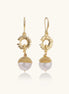 Gold sunburst charm earrings with baroque pearl drops on French hooks against cream background