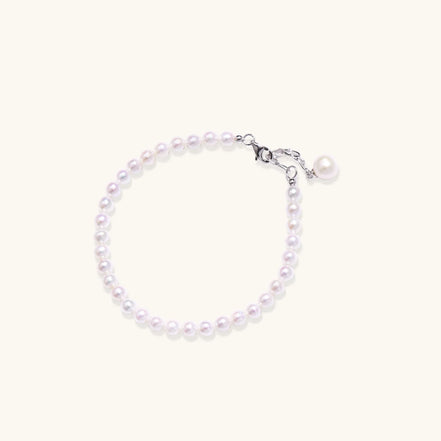 Delicate freshwater pearl bracelet with rhodium-plated silver clasp and single pearl drop charm on cream background