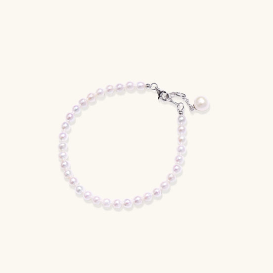 Delicate freshwater pearl bracelet with rhodium-plated silver clasp and single pearl drop charm on cream background