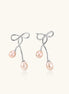 Rhodium-plated silver earrings with organic vine curves and two peachy freshwater pearls on cream background