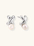 Rhodium-plated silver earrings with twisted X design and freshwater pearl drops on beige background
