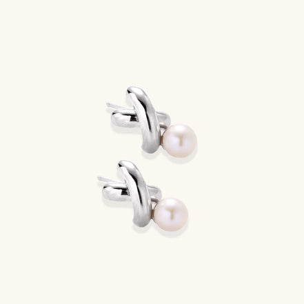 Rhodium-plated silver earrings with twisted X design and freshwater pearl drops on beige background