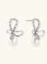 Silver bow-shaped stud earrings with baguette crystals and dangling white freshwater pearls on cream background