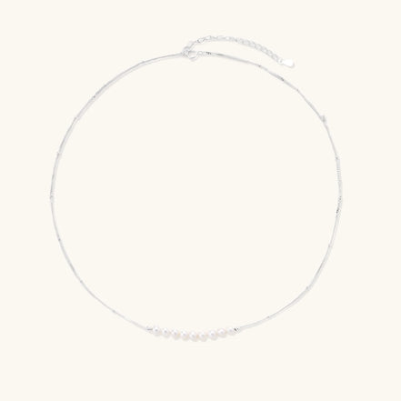 Delicate sterling silver chain necklace with small freshwater pearls arranged in a curved smile arc on cream background.