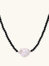Beaded black agate necklace with iridescent baroque freshwater pearl centerpiece on cream background.