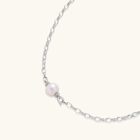 Dainty rhodium-plated silver chain necklace with centered 10mm freshwater pearl and crystal accents on cream background