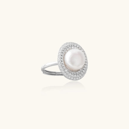 Silver ring with lustrous white pearl center surrounded by sparkling crystal halo on light background.
