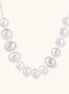 Graduated pearl-finish silver discs forming an organic bubble bib necklace on delicate chain against cream background.