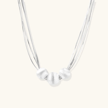 Sterling silver multi-strand necklace with three brushed round beads on cream background