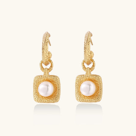 Pair of gold vermeil hoop earrings with textured square frames holding freshwater pearls on cream background